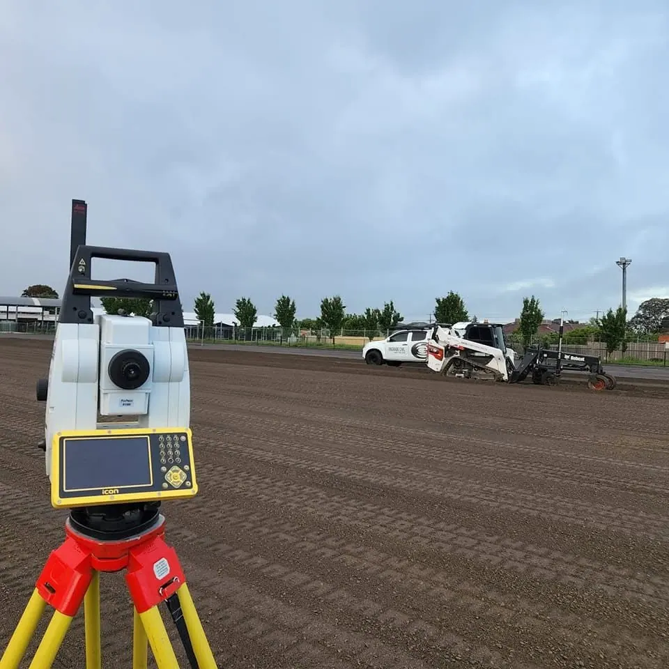 Survey instrument on a tripod with an Ongrade Civil skid steer grading behind
