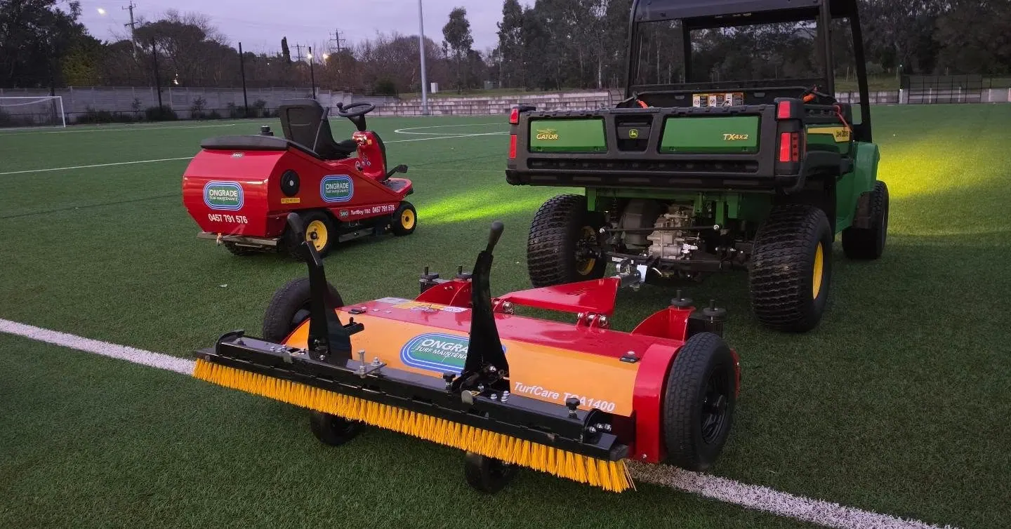 Ongrade branded sweeper and utility vehicle on a floodlit synthetic sports field at dusk