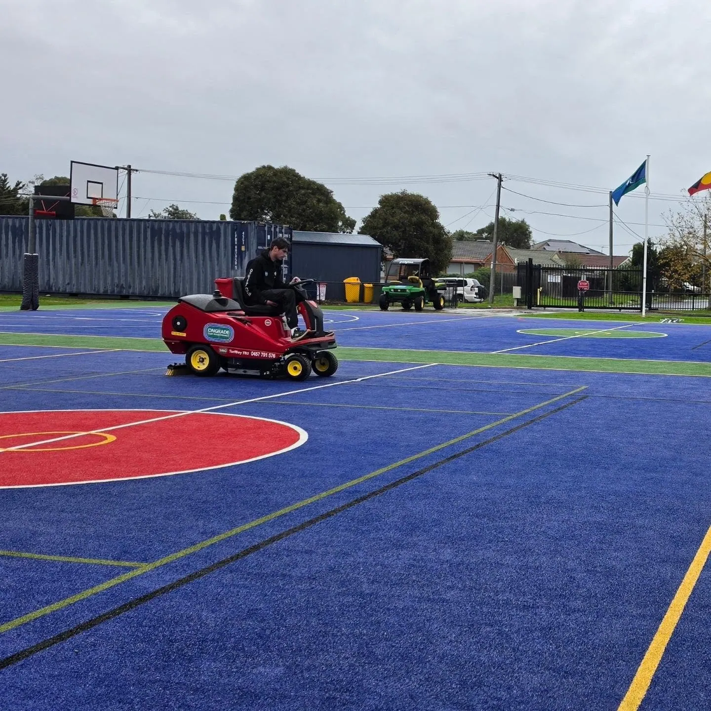 Ongrade operator sweeping a blue and red multi-sport synthetic school court